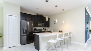 A modern kitchen with dark cabinets, stainless steel appliances, and a white island with bar stools. - Last Minute Disney Getaway! Private Pool & Themed Bedrooms. Book Now! #40229 (Orlando)