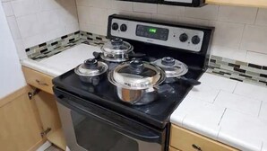 Une cuisine avec un fourneau noir, trois casseroles sur les brûleurs, un four à micro-ondes au-dessus du fourneau et un pare-feu en carreaux.