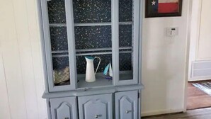 Un petit meuble en bois bleu clair, doté de portes en verre, contenant un vase blanc et un pichet bleu et blanc.