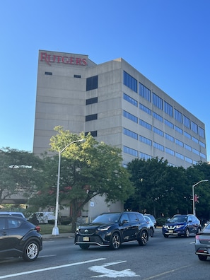 A building with a sign reading 'RUTGERS' on the facade, surrounded by parked cars and a tree with green leaves. - Luxury 2Kings Bedroom Near EWR airport/NYC manhattan (Newark)