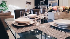 Een moderne keuken met donkere kastjes, roestvrijstalen apparatuur en een eethoek met een glazen tafel voor vier personen.