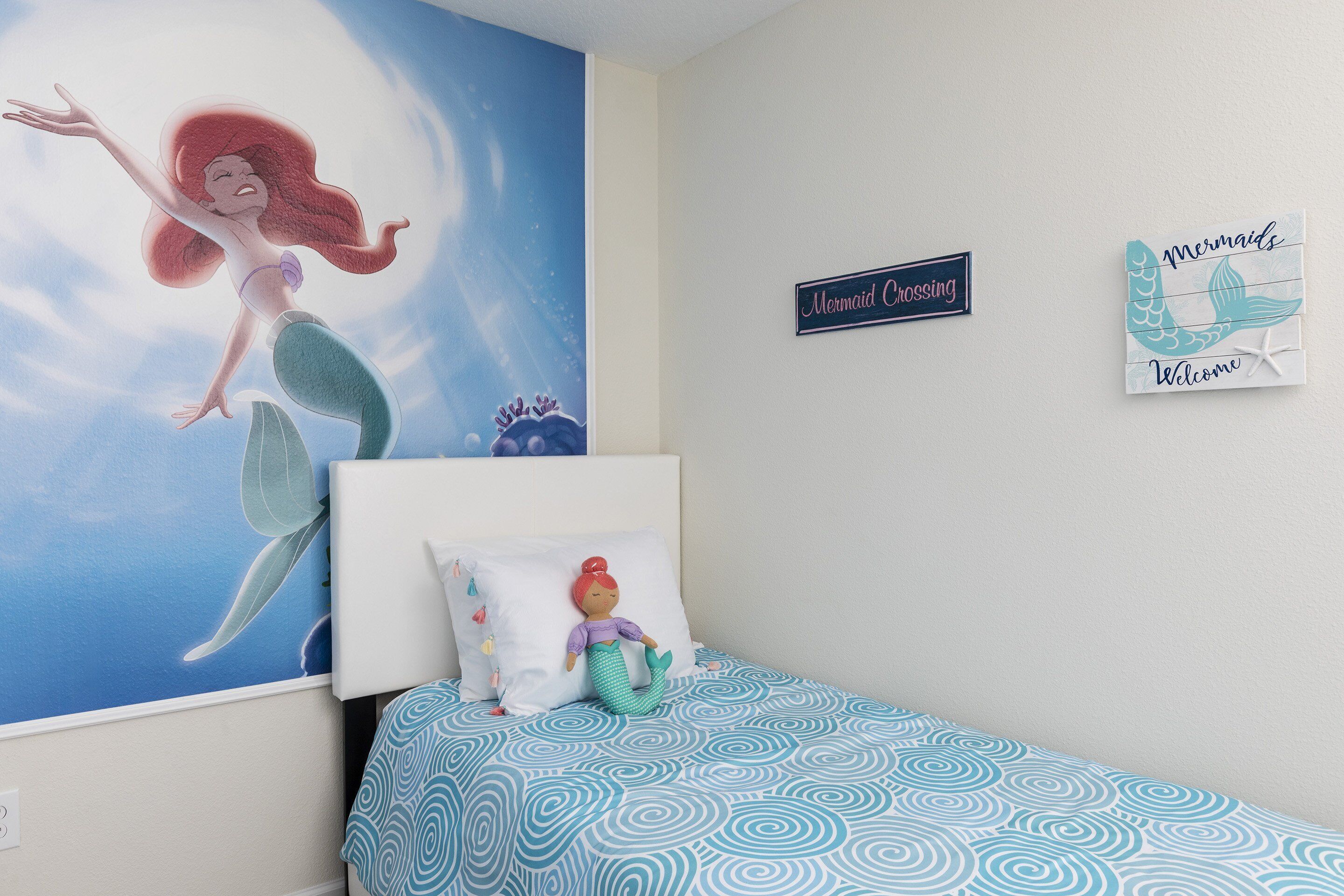 A bedroom with a mural of a mermaid, a plush toy, and two wall decorations.