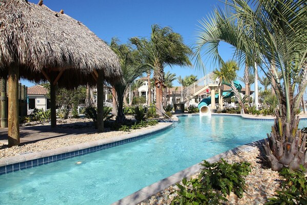 Relax by the resort pool surrounded by lush vegetation and a thatched-roof structure.