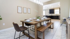 A dining area with a wooden table set for four, surrounded by chairs. A kitchen is visible in the background with dark cabinets and a window. - Last Minute Disney Getaway! Villa with Private Pool & Hot Tub. Book Now! #43253 (Orlando)