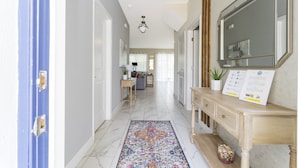 A hallway with a marble floor, a blue door, a wooden console table with a mirror and informational cards, and a patterned rug. - Last Minute Disney Getaway! Villa with Private Pool & Hot Tub. Book Now! #43253 (Orlando)