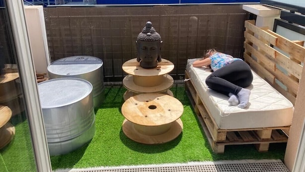 Ein kleiner, abgeschlossener Außenbereich mit grüner Kunstrasenfläche, einer Holzbank, einem Metalltopf und einer kleinen Buddha-Statue.