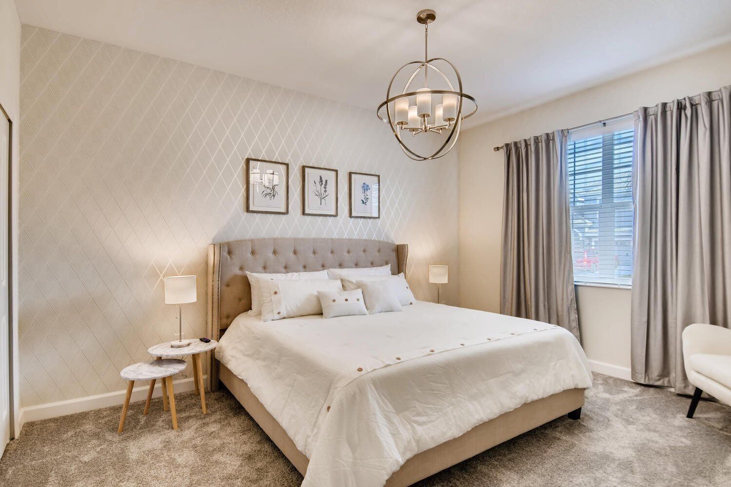 Ruime slaapkamer met een groot bed, een kroonluchter, een klein nachtkastje en uitzicht op de straat.