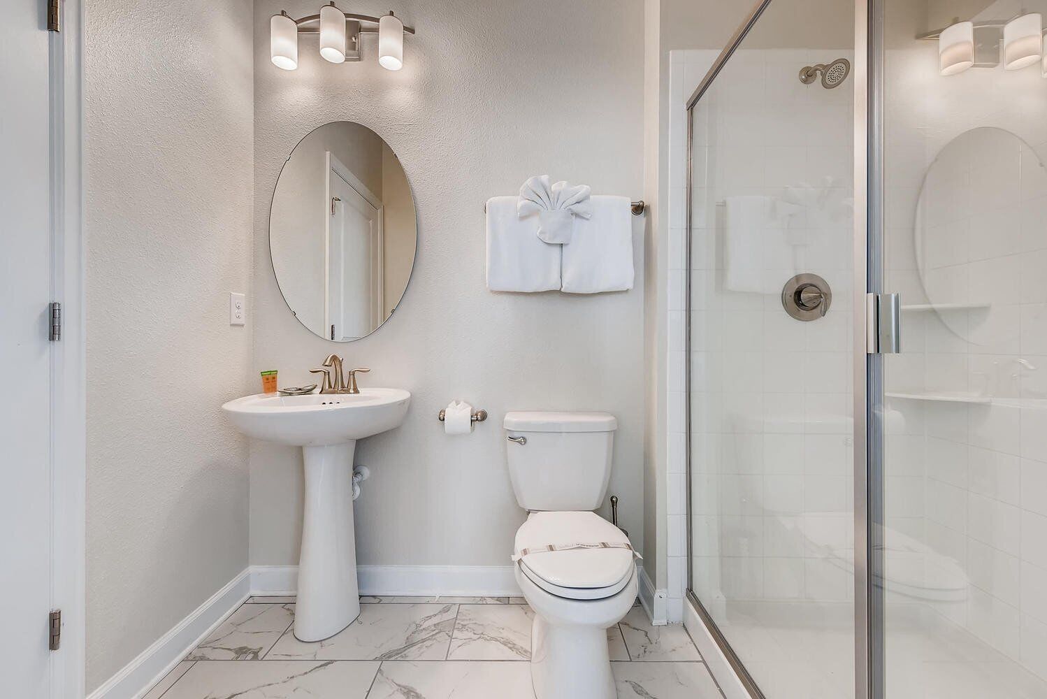 Un baño con lavamanos pedestal, inodoro y cabina de ducha con mampara de vidrio.