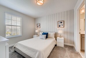Una camera da letto con un letto grande, due comodini con lampade, una finestra con tende e una porta che dà su un'altra stanza.