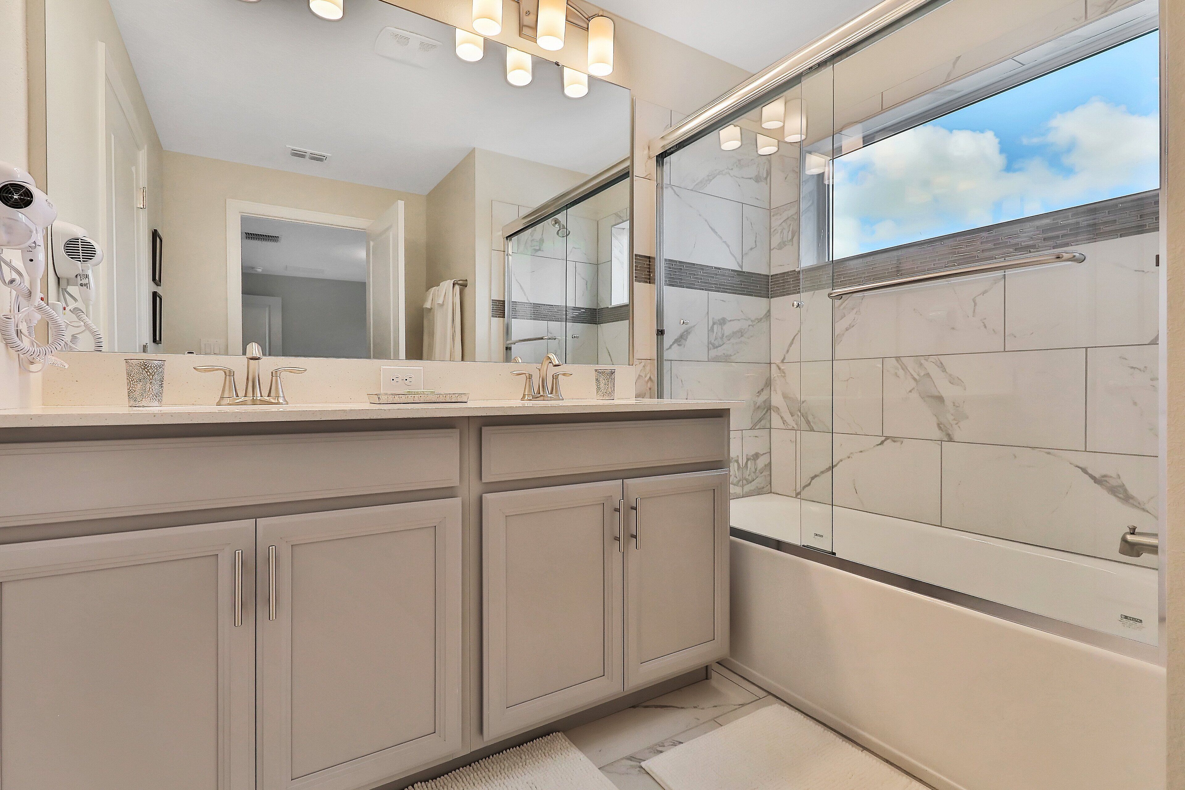 A modern bathroom with a large mirror, a shower with glass doors, and a vanity with a hairdryer.