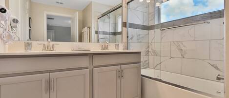 A modern bathroom with a large mirror, a shower with glass doors, and a vanity with a hairdryer.
