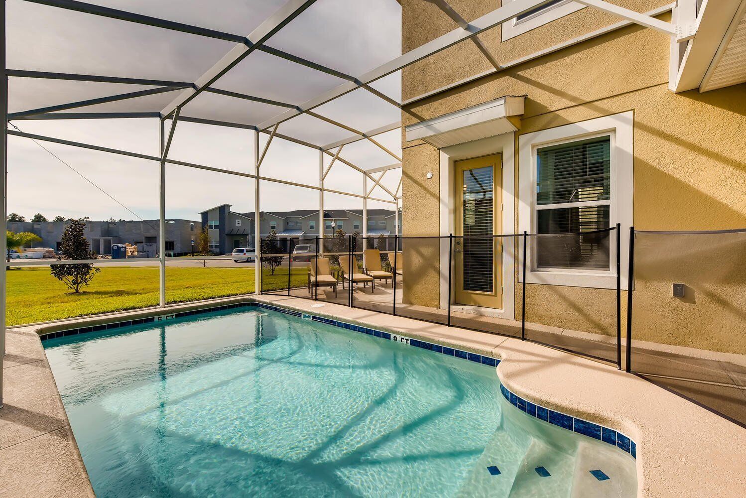 Una piscina con zona techada, rodeada por una cerca, y un edificio de fachada amarilla.