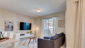 Een moderne woonkamer met een bank, een eettafel en een aan de muur bevestigde televisie.
