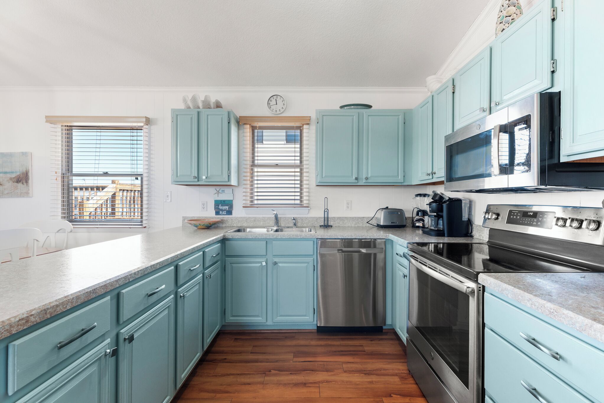 Una cocina con armarios color turquesa, electrodomésticos de acero inoxidable y piso de madera.