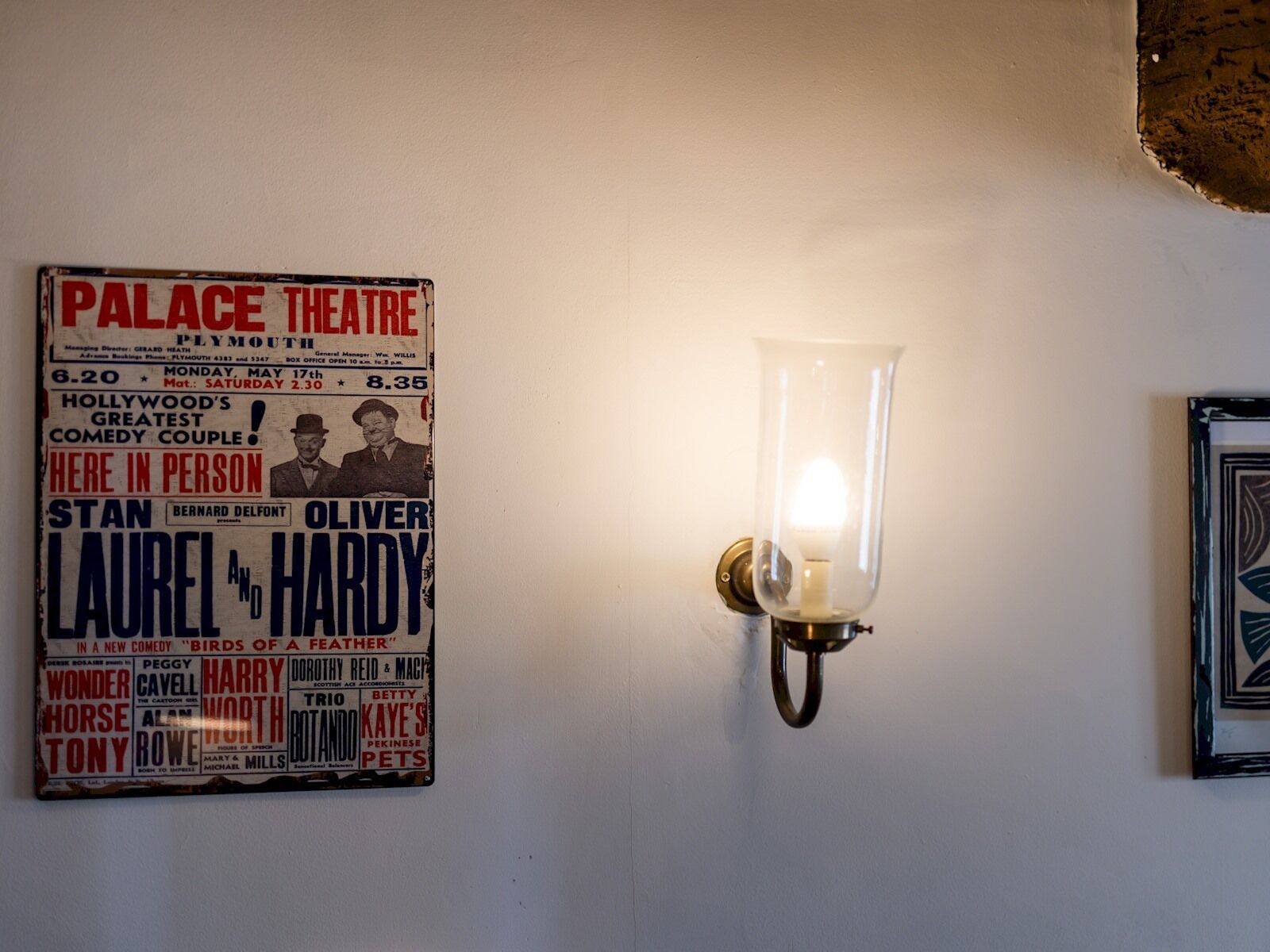 A vintage theater poster with a clear glass light fixture beside it.