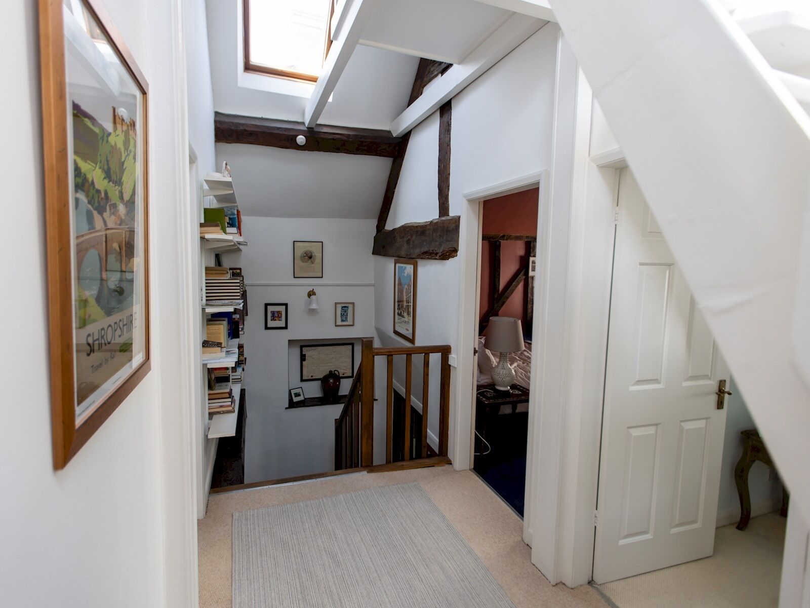 A narrow hallway with a sloped ceiling, wooden beams, and a small staircase leading to a room.