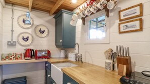 A kitchen with wooden cabinets, a sink, a toaster, and various kitchen utensils. - The Jenny Wrennery (Rugeley)