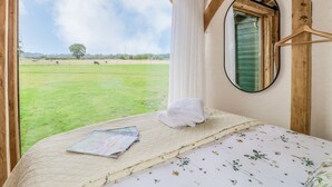 A bedroom with a large window, a bed with a quilt and a magazine, and a mirror on the wall. - The Jenny Wrennery (Rugeley)