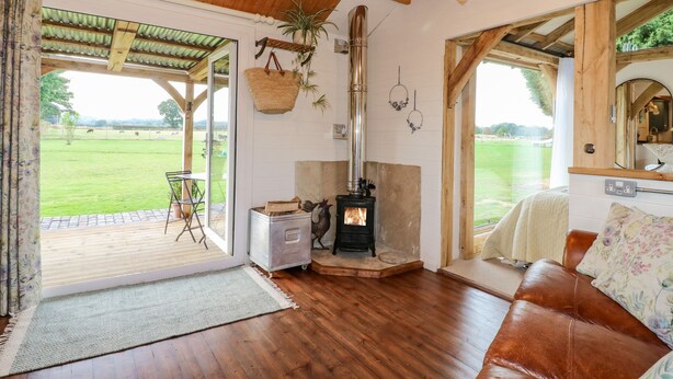 A cozy room with a wooden ceiling, a fireplace, a leather sofa, and a view of a green field. - The Jenny Wrennery (Rugeley)