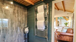 A bathroom with a wooden wall, a towel rack, and a shower area. - The Jenny Wrennery (Rugeley)