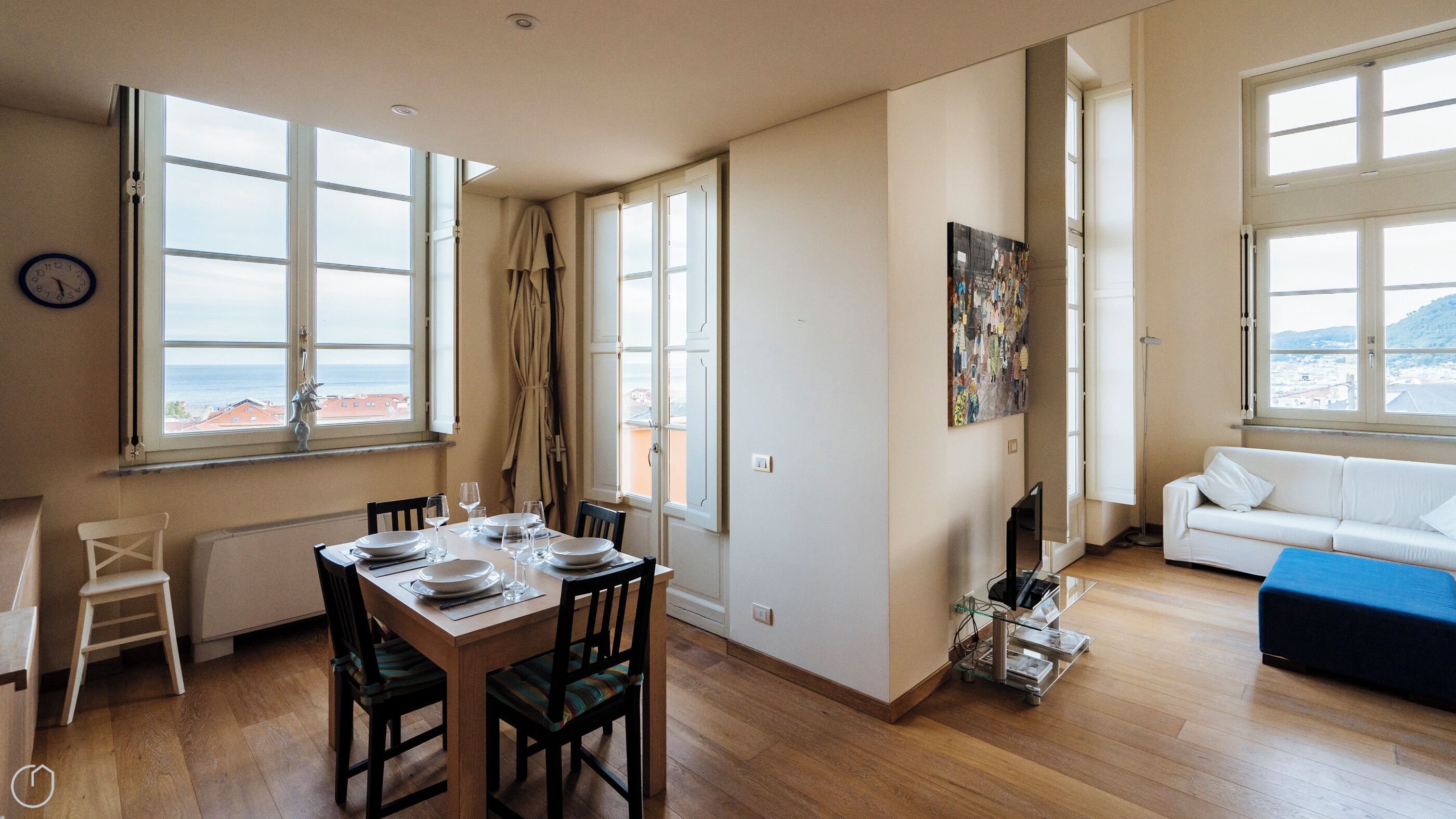 A spacious living room with a large window, a dining area with a table set for four, and a white sofa.
