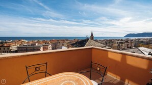 A balcony with a tiled table and chairs, overlooking a coastal town with buildings and a church spire. - Virgilio 2 - Villa Bice (Alassio)
