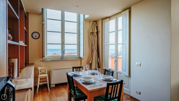 A dining area with a table set for two, a view of the sea, and a clock on the wall. - Virgilio 2 - Villa Bice (Alassio)