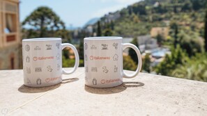Two white mugs with Italian symbols and the text "italianway" on a table with a scenic mountain view in the background.