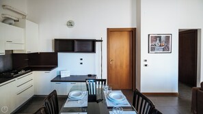 Et lille køkken med hvide skabe, en sort bordplade og et spiseområde med et bord dækket til to.