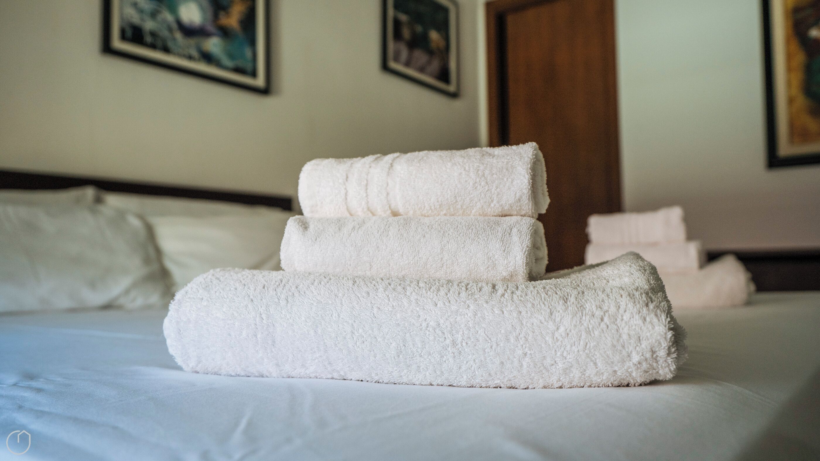 A neatly made bed with a stack of white towels on top.