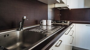 A modern kitchen with a stainless steel sink, two white mugs, a gas stove, and white cabinets. - Viale Hambury 51 (Alassio)