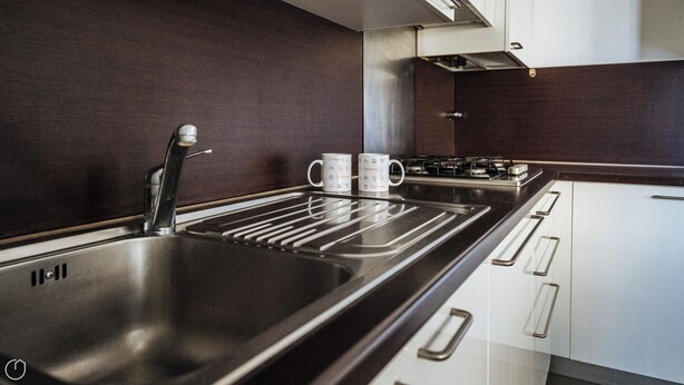 A modern kitchen with a stainless steel sink, two white mugs, a gas stove, and white cabinets.