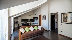 A modern living room with a brown sofa, a dining table, and a kitchen in the background.