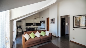 A modern living room with a brown sofa, a dining table, and a kitchen in the background.