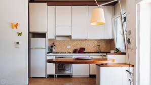 Une cuisine compacte avec des meubles blancs, un four encastré, une cuisinière et un luminaire suspendu.
