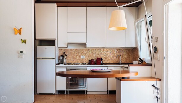A compact kitchen with white cabinets, a built-in oven, a stove, and a hanging light fixture. - Aurelia Harbour 103 (Andora)