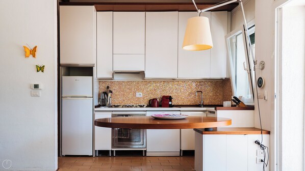 Cocina compacta con armarios blancos, horno empotrado, estufa y lámpara colgante.