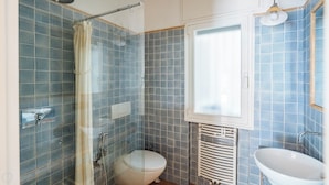 Une salle de bain équipée d’une douche, de toilettes et d’un lavabo, avec des carreaux bleus et une fenêtre.