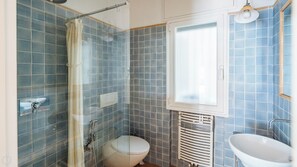 Ein Badezimmer mit Dusche, Toilette und Waschbecken, ausgestattet mit blauen Fliesen und einem Fenster.