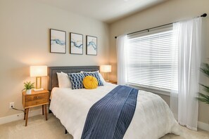 Une chambre à coucher comprenant un lit, deux tables de chevet, une commode, une lampe, une plante et une fenêtre avec des stores.