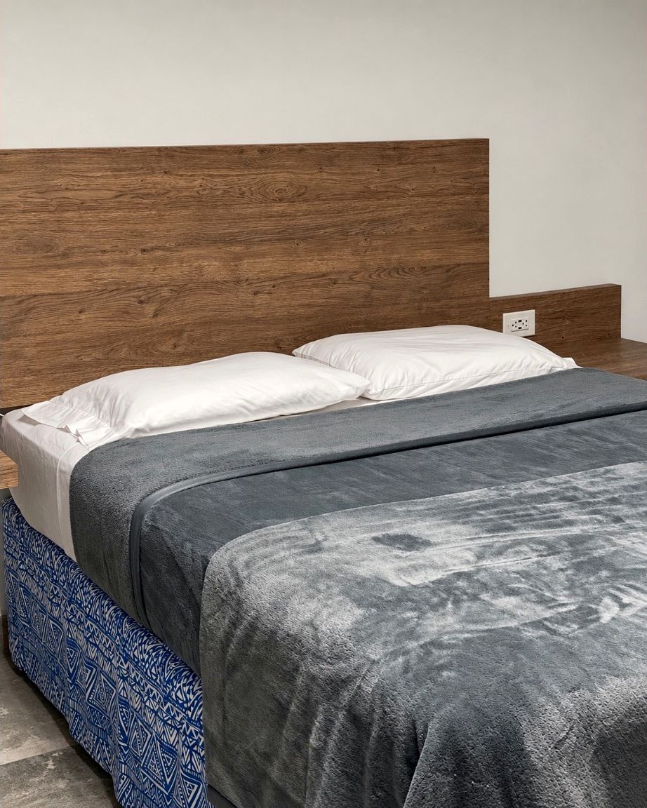 A bed with a wooden headboard, white pillows, and a grey blanket.