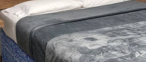 A bed with a wooden headboard, white pillows, and a grey blanket.