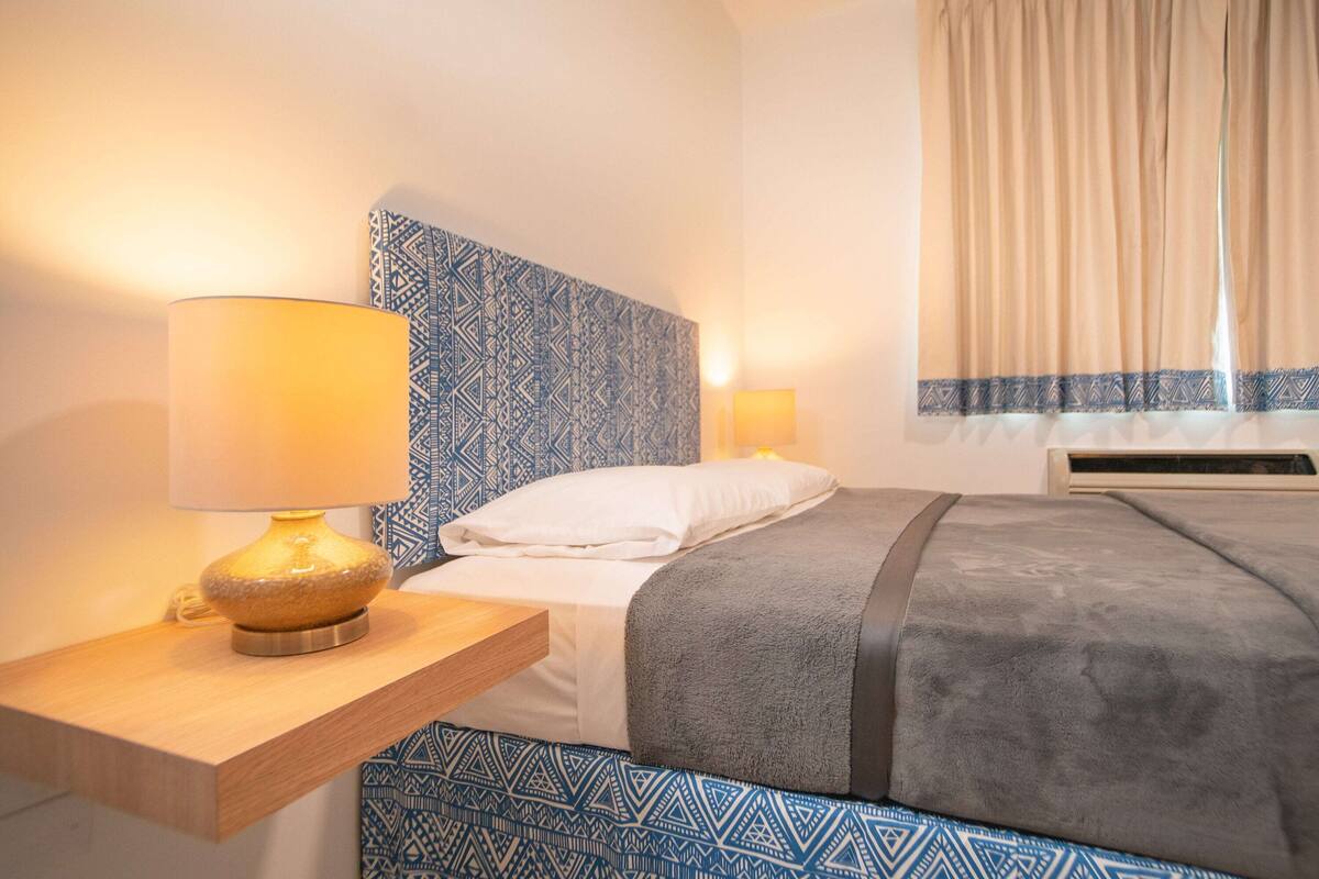 Ein Hotelzimmer mit Bett, Nachttisch, Lampe und einem gemusterten Kopfteil.
