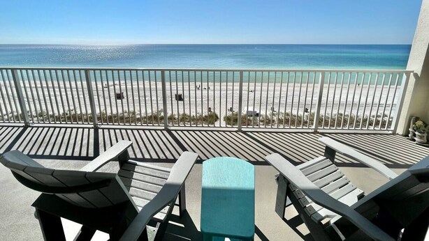 Een balkon met uitzicht op het strand, met een leuning en twee ligstoelen.