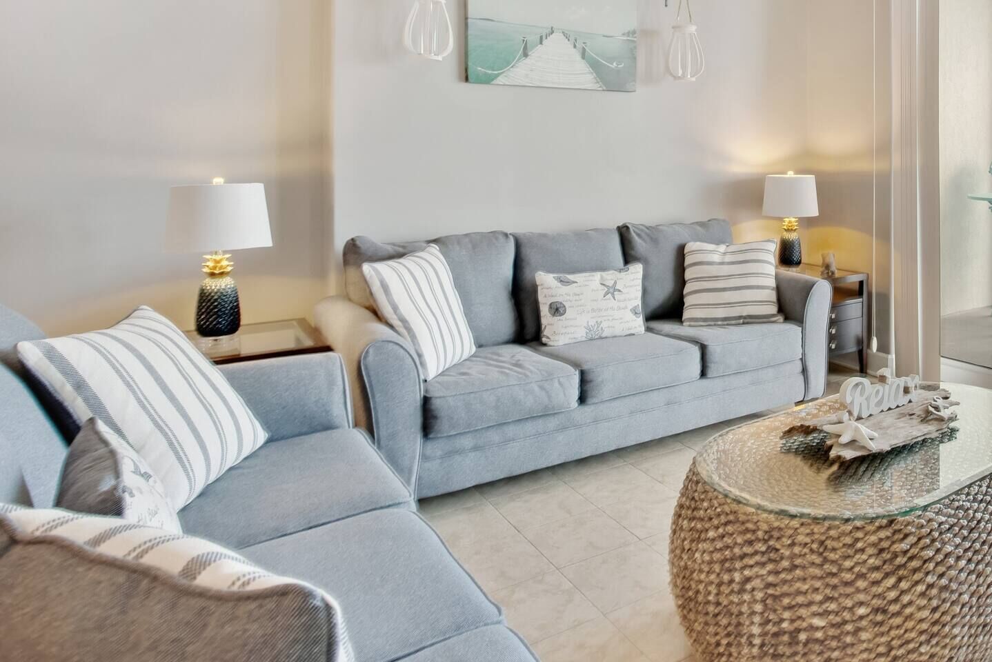Un salon moderne avec un canapé gris, deux tables d’appoint avec des lampes, une table basse en verre et un objet décoratif posé sur la table.