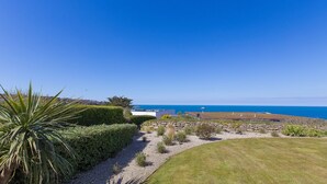 Une propriété située sur la côte, offrant une vue dégagée sur la mer, avec un mur en pierre et un chemin menant à un bâtiment blanc.
