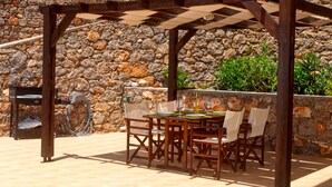 An outdoor patio with a wooden pergola, stone wall, and a table set for dining.