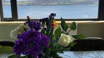 Eine Vase mit Blumen auf einem Tisch neben einem Fenster mit Blick auf einen See.