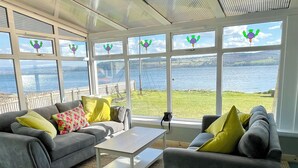 Une véranda aménagée avec un canapé et des fauteuils, une table basse et une vue sur la mer.