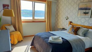 Une chambre à coucher avec un lit, une table de chevet, une lampe et une fenêtre avec des rideaux.